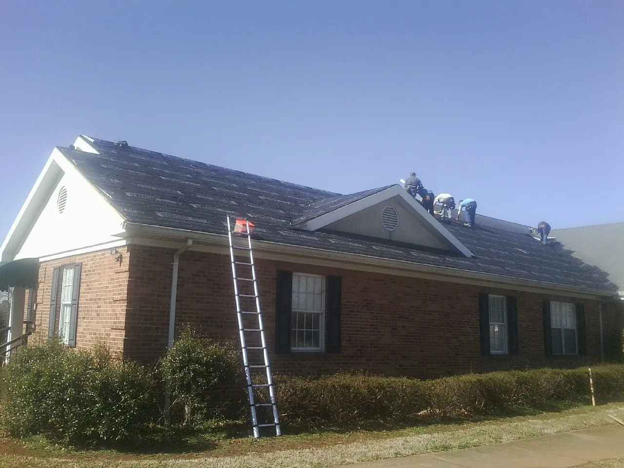Crew tearing shingles off a brick ranch roof with a ladder set — Emergency Roof Repair work by our crew in Pine Plains