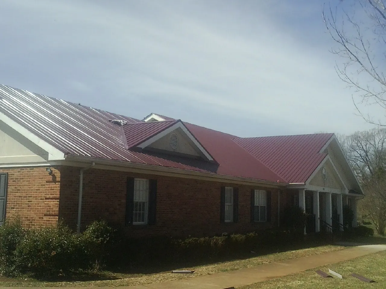 Red metal roof with gabled entries on a long brick building, from a Hail Damage Roof Repair job in Pine Plains