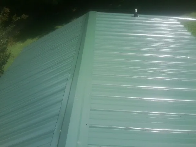 New green metal panels meeting at the ridge of a roof — Flat Roof Repair work by our crew in Pine Plains