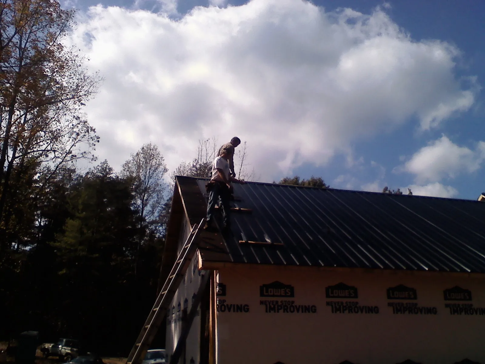 Roofer fastening dark metal panels high against a cloudy sky, from a Roof Inspection job in Pine Plains