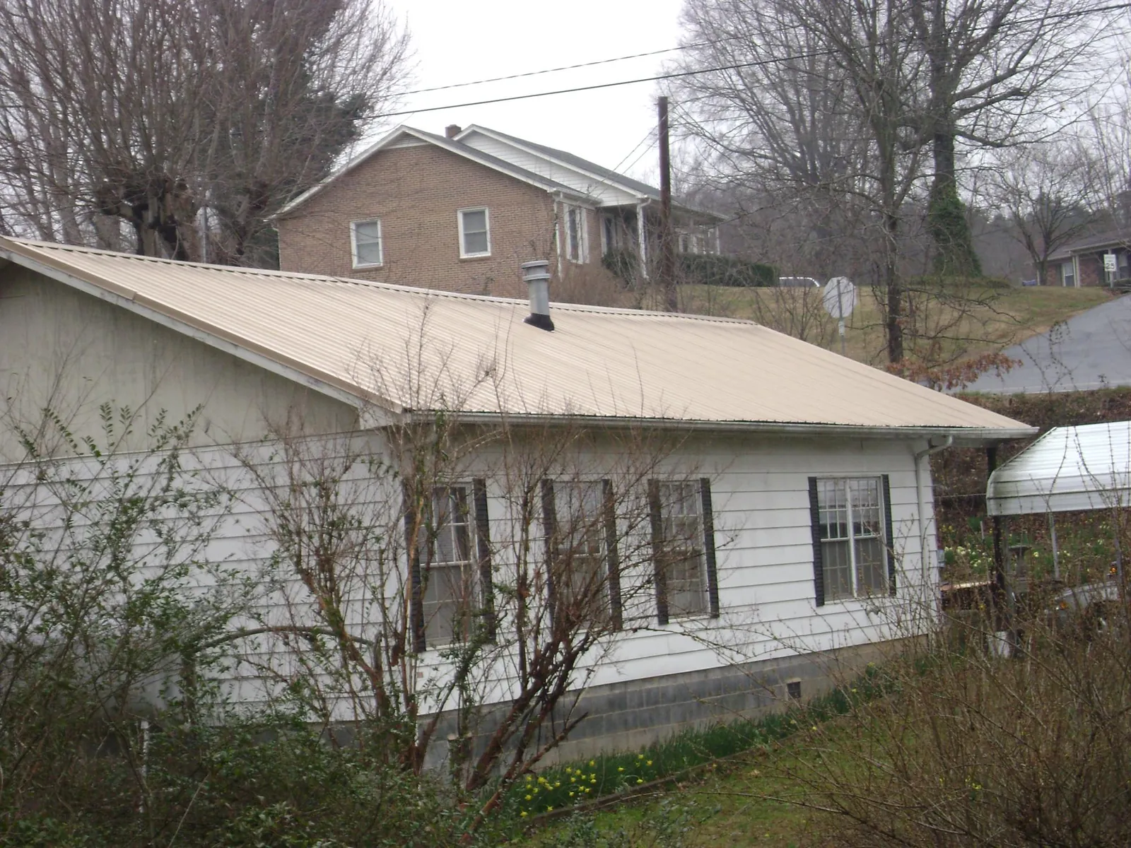 Tan metal roof on a white sided house set into a hillside — Commercial Roofing by Roofing Brothers in Pine Plains