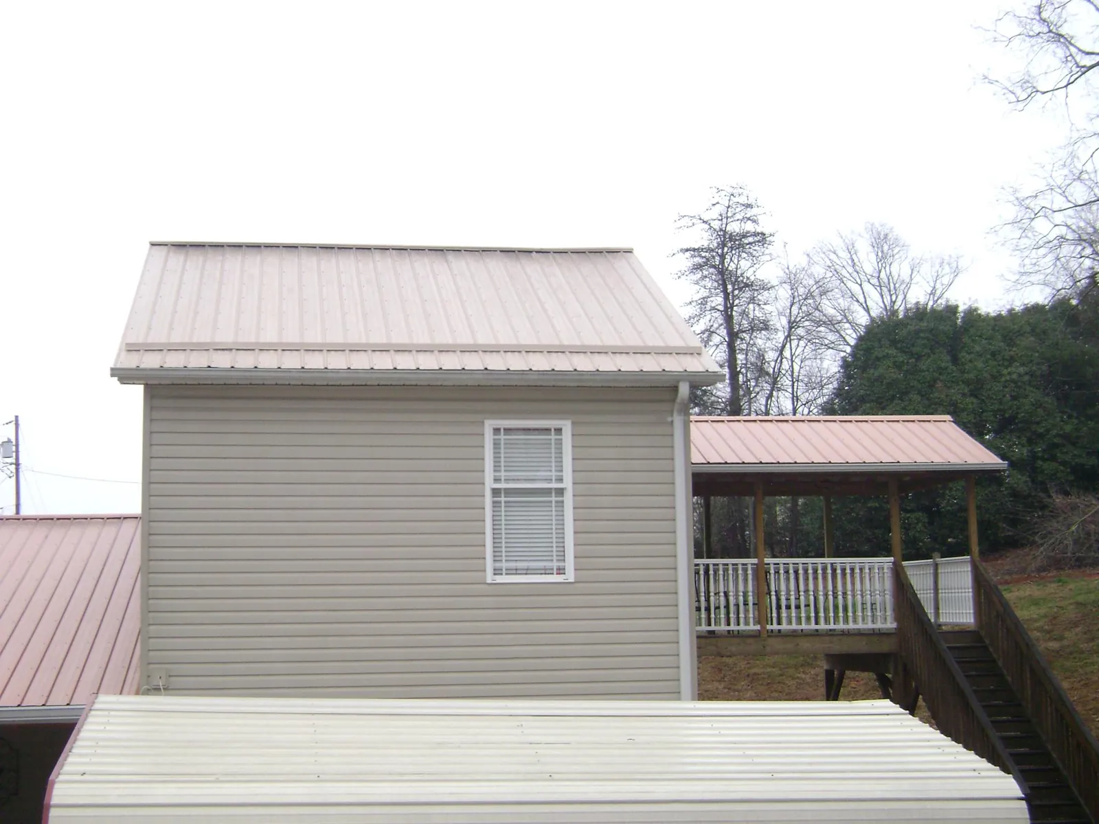 Tan metal roofs on a two story addition and attached porch, from a Roof Replacement job in Pine Plains